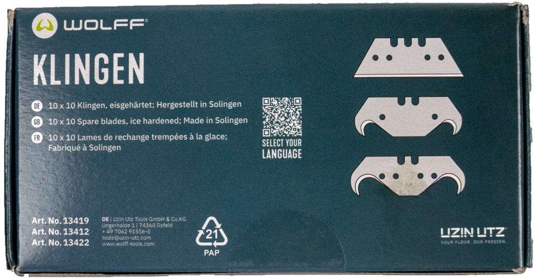 Close-upfoto van een rechthoekige kartonnen doos met Wolff-vervangingsmesjes voor vloerwerktuigen. De donkergroene verpakking toont linksboven het merklogo 'WOLFF' en links het grote witte woord 'KLINGEN'. Aan de rechterkant staan drie gestileerde mesillustraties; ertussen staat een kleine QR-code met de tekst 'SELECT YOUR LANGUAGE'. Meertalige productinformatie vermeldt in het Duits, Engels en Frans '10 x 10 reserve mesjes, ijsgehard; Made in Solingen'. Linksonder staan drie artikelnummers en contactgegevens van de fabrikant, en het recycling symbool '21 PAP' bevindt zich onderaan. De doosranden vertonen lichte gebruikssporen. Algemene weergave van een nette productverpakking op witte achtergrond.
